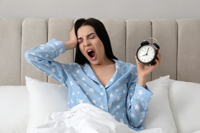 Photo of Overslept woman with alarm clock in bed. Being late concept