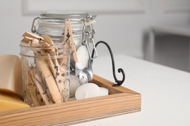 Photo of Wooden tray with many clothespins, candles and soap bars on white table indoors, space for text