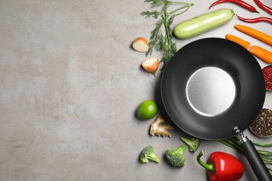 Photo of Empty iron wok surrounded by raw ingredients on grey table, flat lay. Space for text