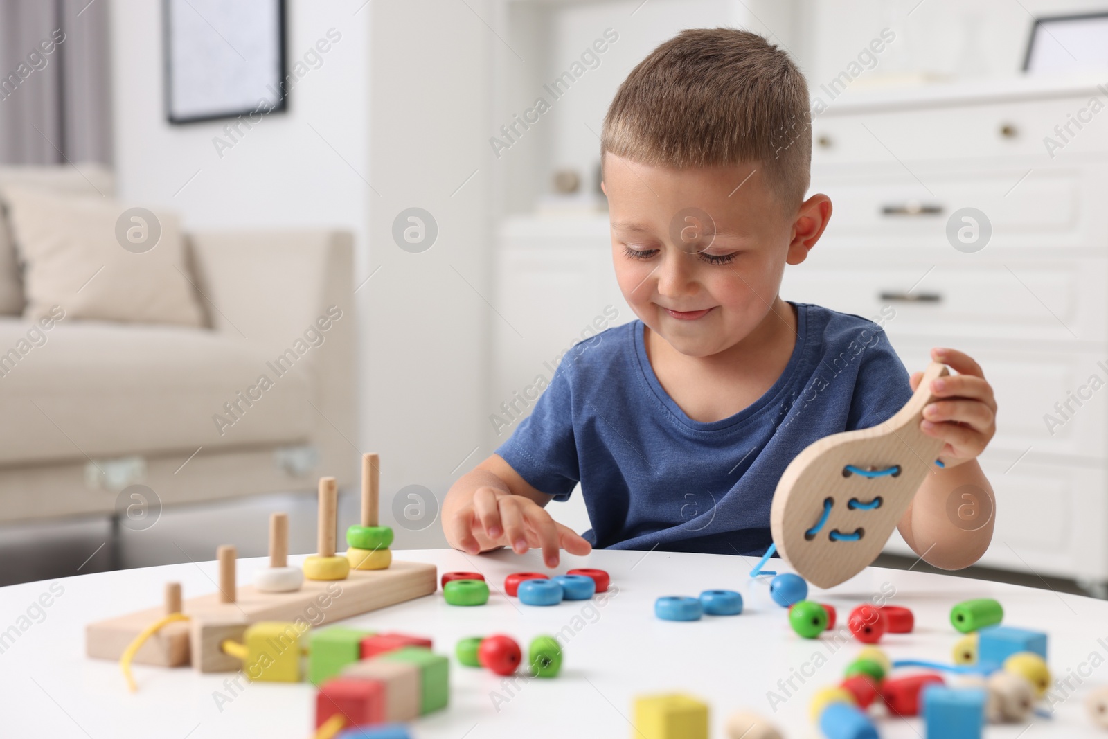 Photo of Motor skills development. Little boy playing with wooden lacing toy at white table indoors