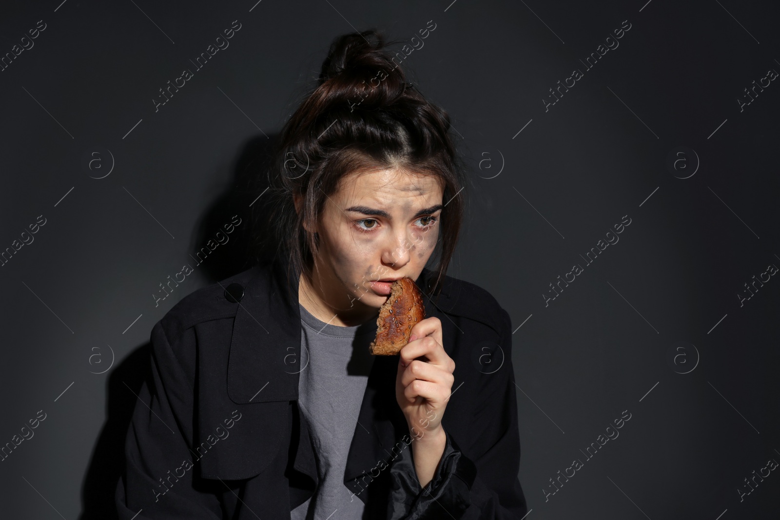 Photo of Poor woman with piece of bread on dark background, space for text