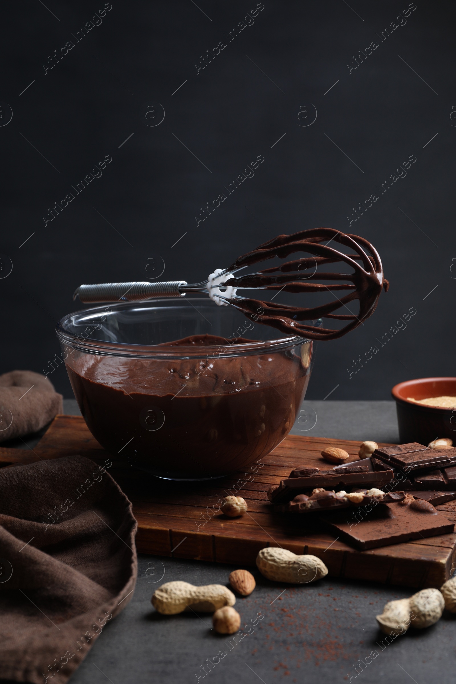 Photo of Bowl of chocolate cream, whisk and ingredients on gray table against dark background, space for text