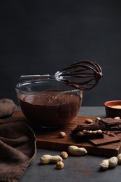 Bowl of chocolate cream, whisk and ingredients on gray table against dark background, space for text