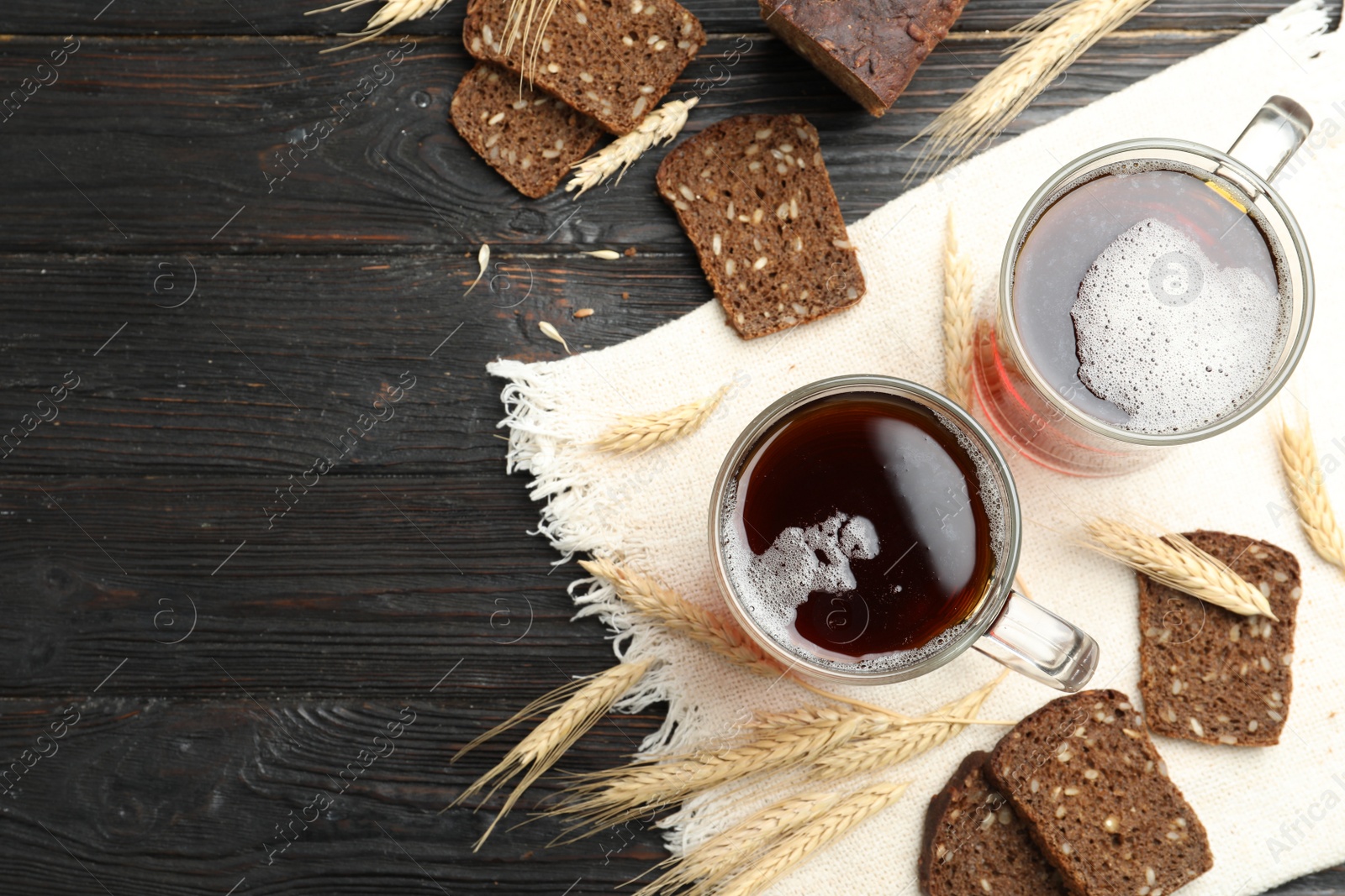 Photo of Mugs of delicious kvass, spikes and bread on wooden table, flat lay. Space for text