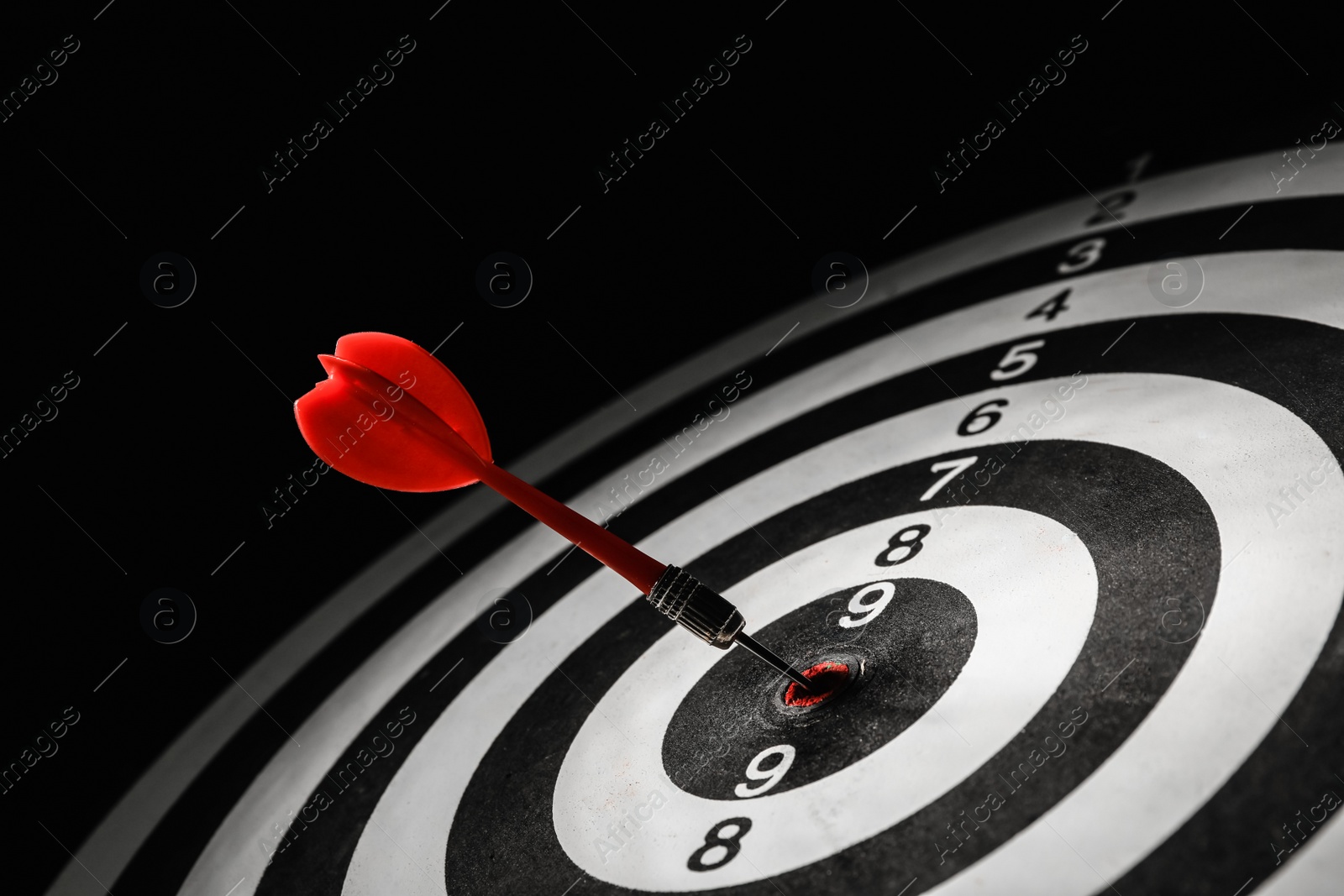 Photo of Red arrow hitting target on dart board against black background