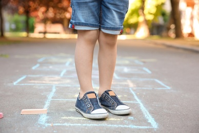 Photo of Little child playing hopscotch drawn with colorful chalk on asphalt