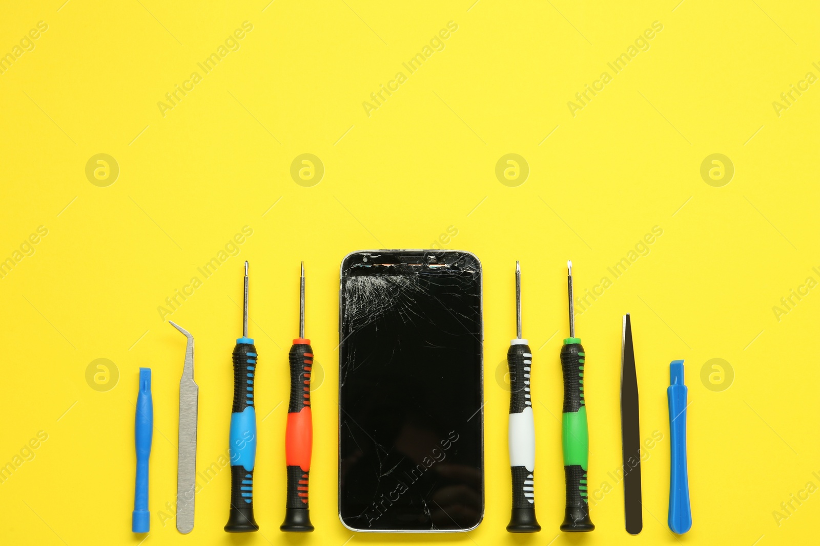 Photo of Damaged smartphone and repair tool set on yellow background, flat lay. Space for text