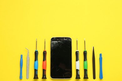 Damaged smartphone and repair tool set on yellow background, flat lay. Space for text