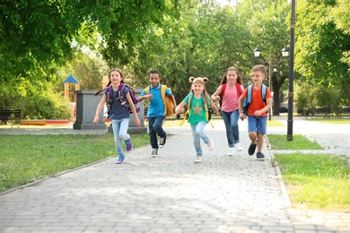 Photo of Cute little children with backpacks running outdoors. Elementary school