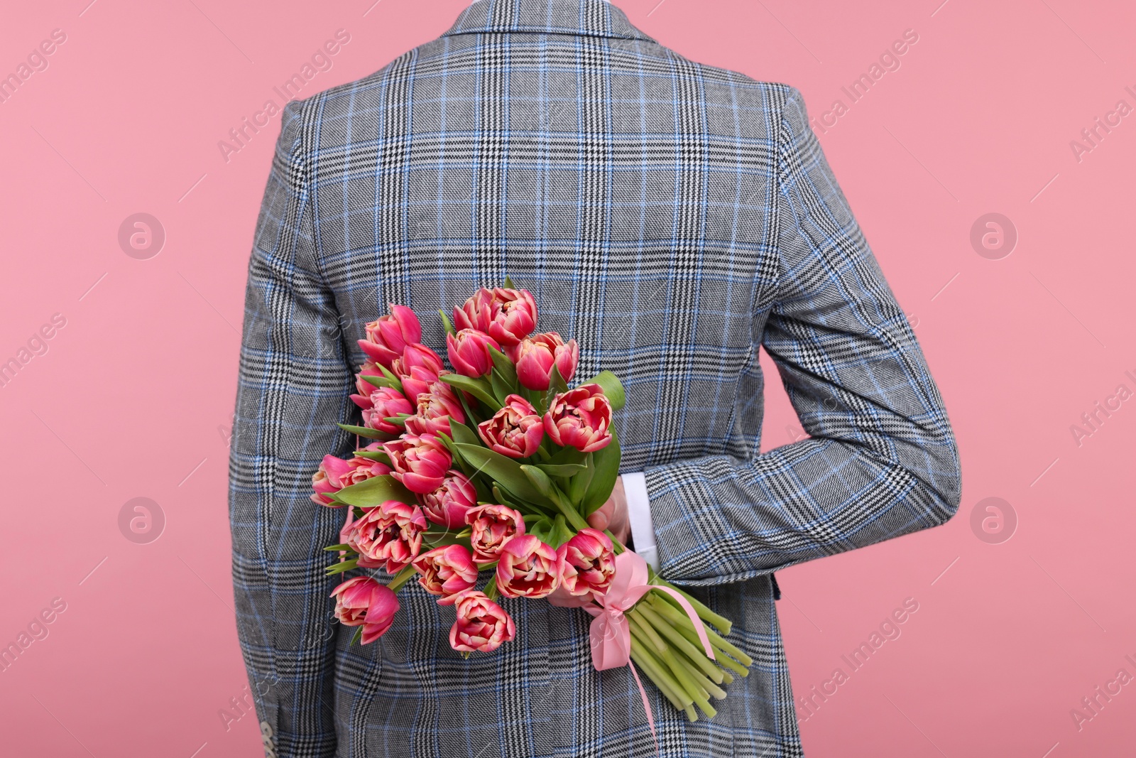 Photo of Man hiding beautiful bouquet on pink background, back view