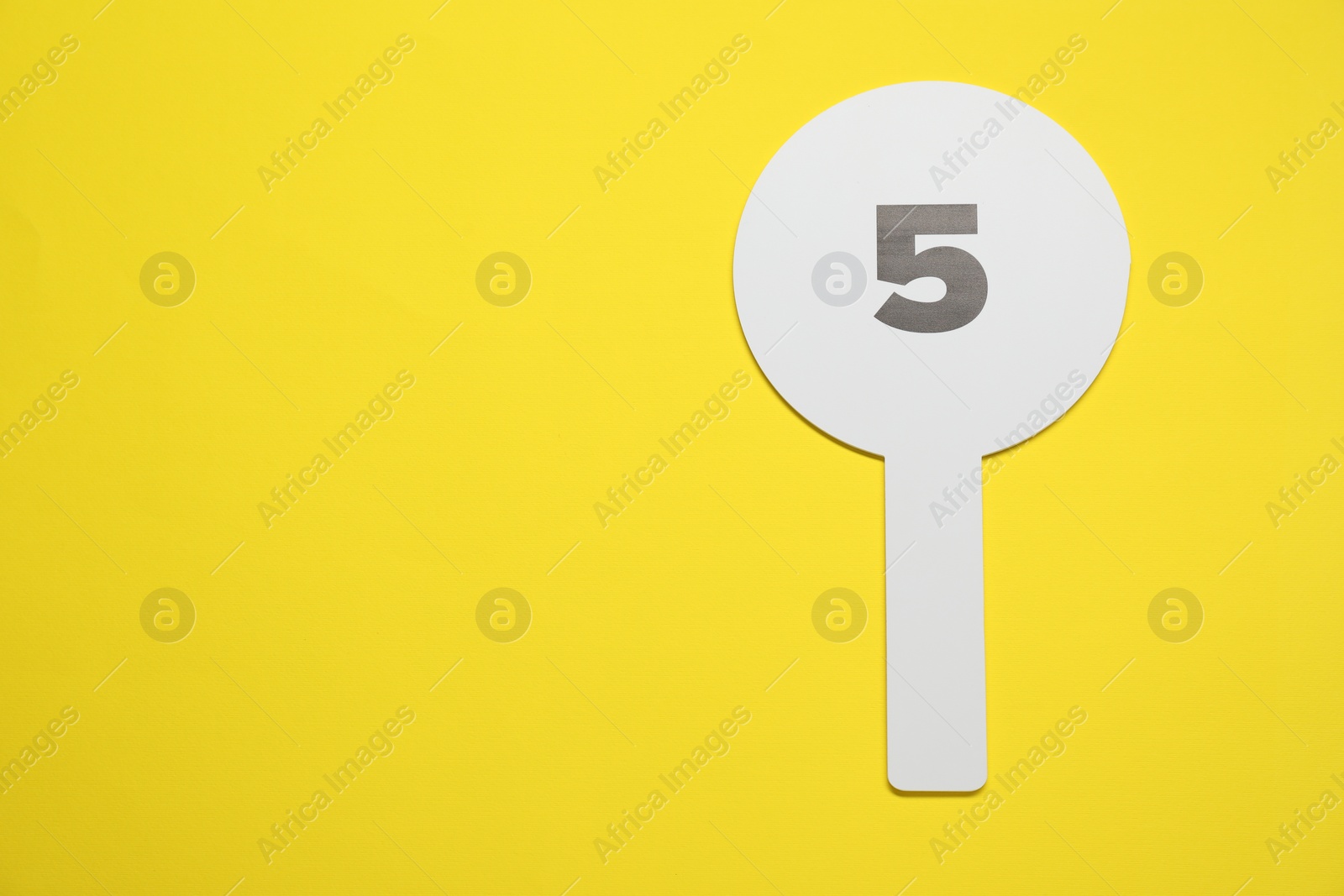 Photo of Auction paddle with number 5 on yellow background, top view. Space for text