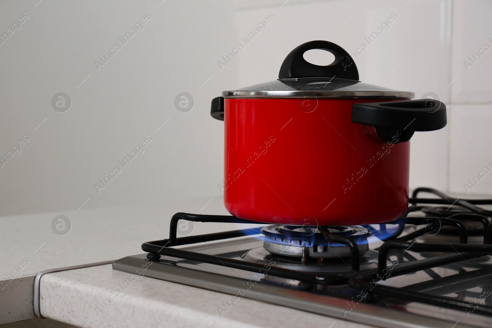 Photo of Red pot on stylish kitchen stove with burning gas, space for text