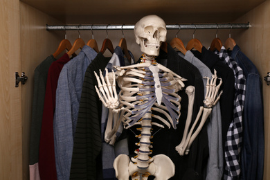 Photo of Artificial human skeleton model among clothes in wardrobe