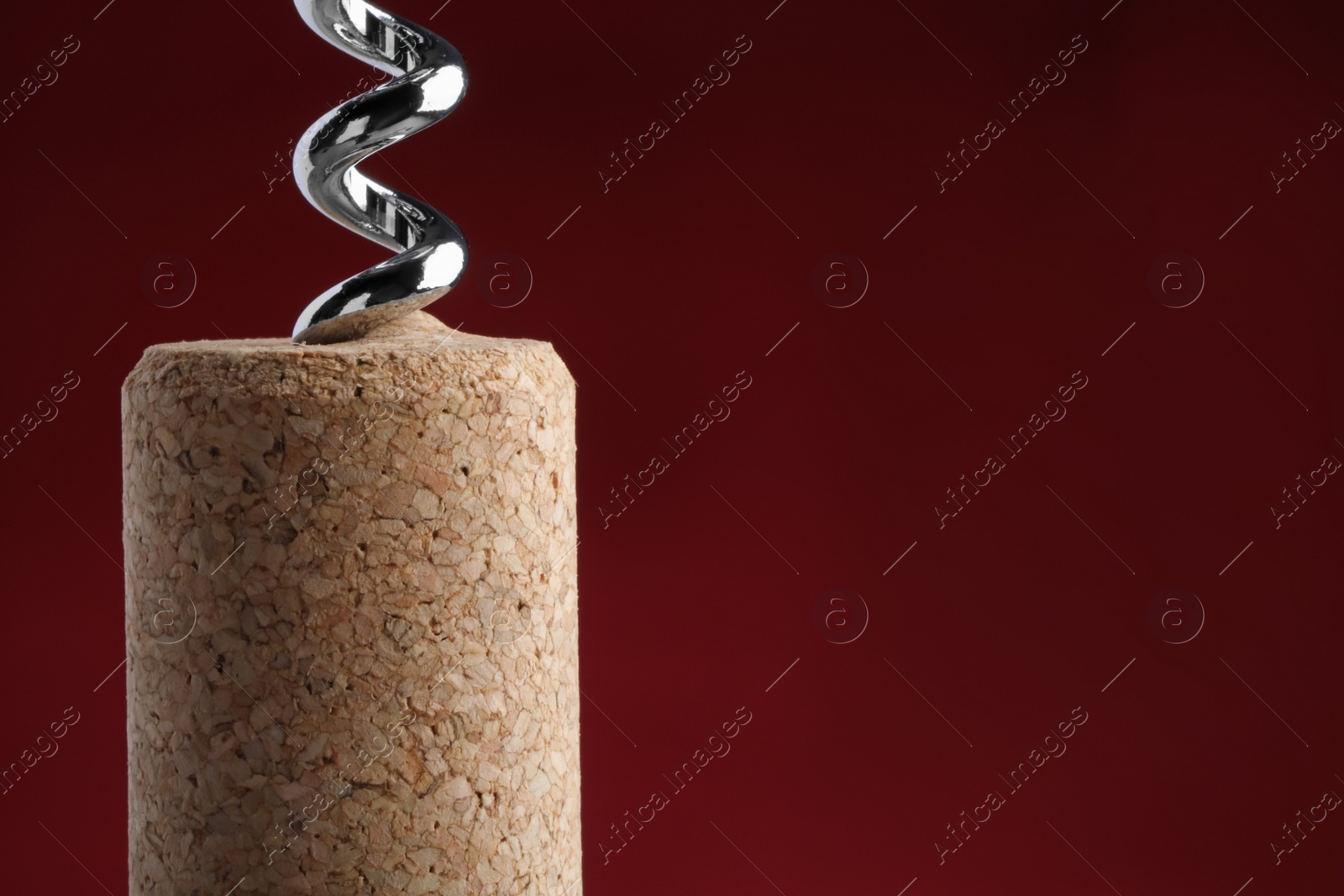 Photo of Corkscrew with wine cork on dark red background, closeup. Space for text