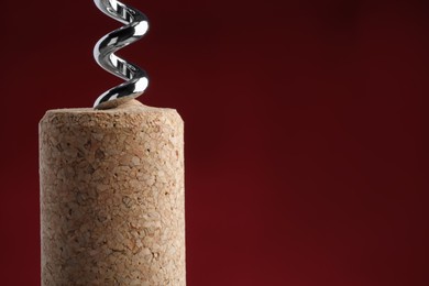 Photo of Corkscrew with wine cork on dark red background, closeup. Space for text