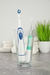 Photo of Electric toothbrushes in glass on light grey marble table