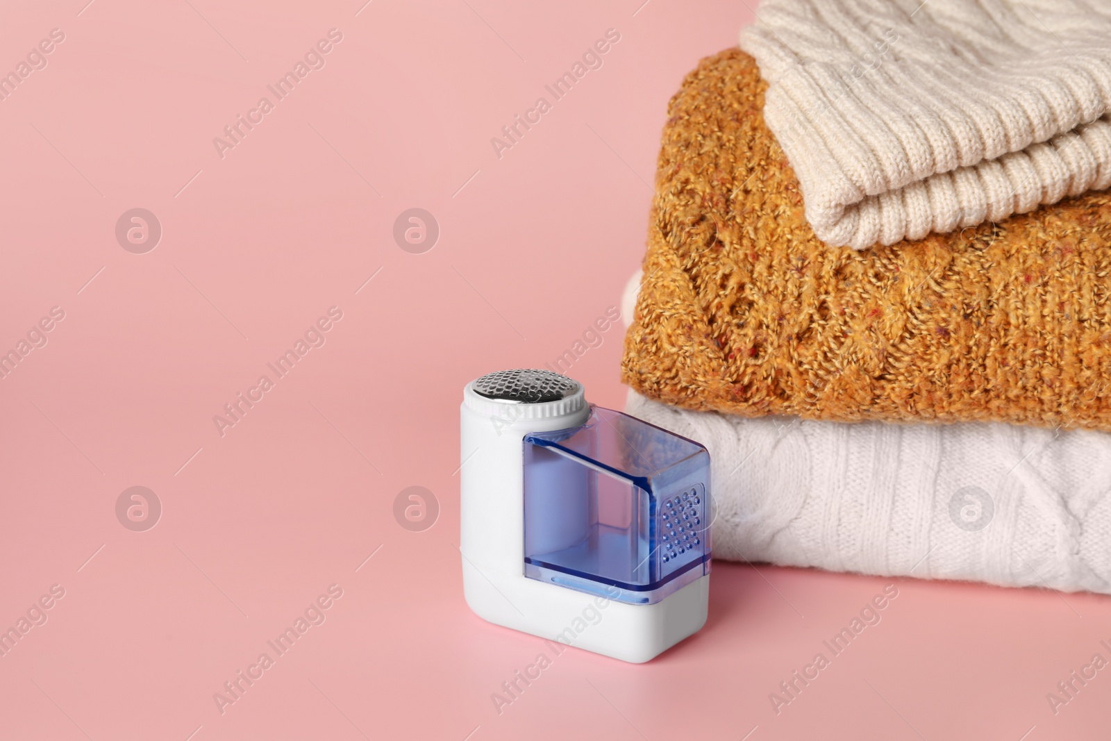 Photo of Modern fabric shaver and knitted clothes on pink background, space for text