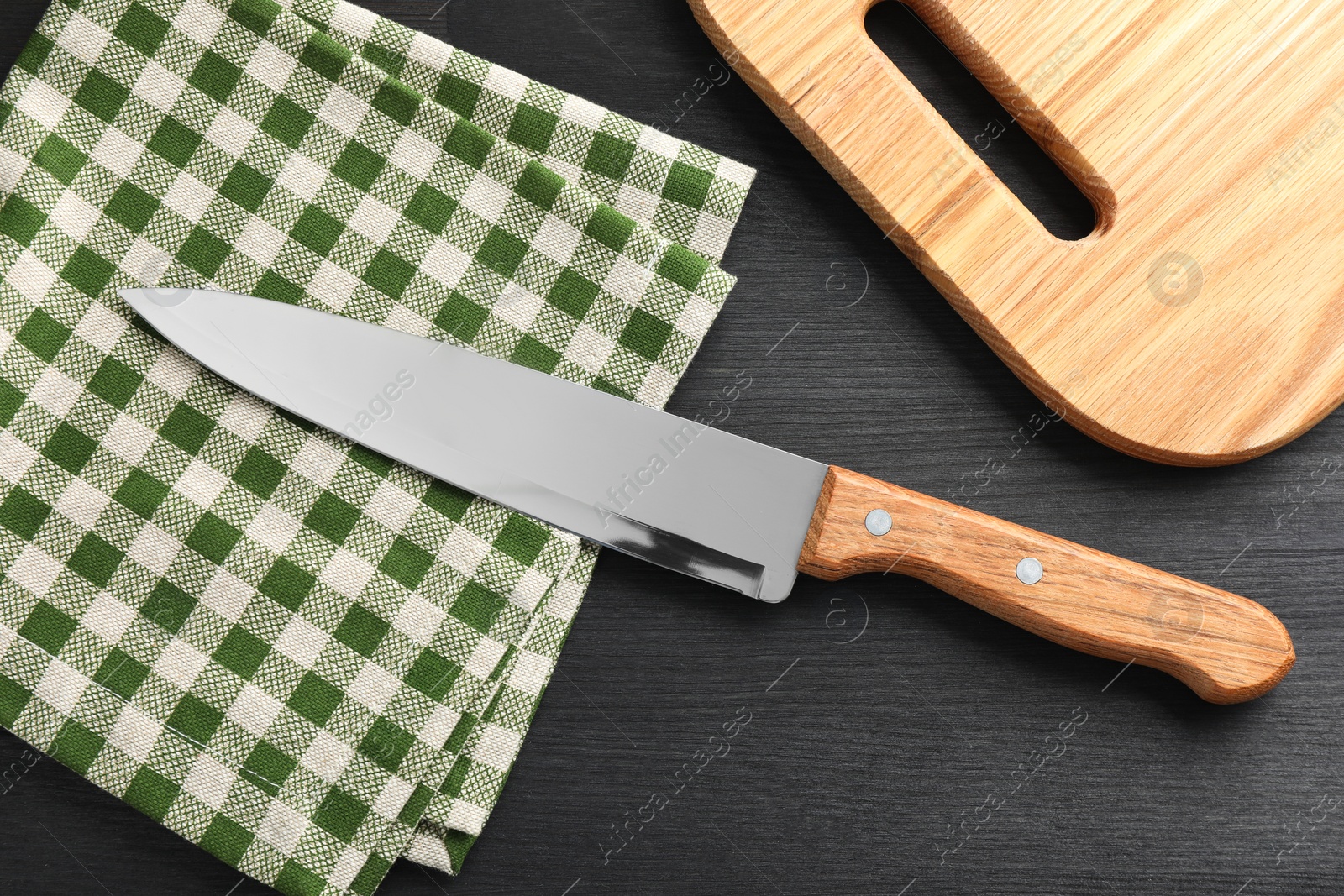 Photo of One sharp knife, napkin and board on black wooden table, flat lay