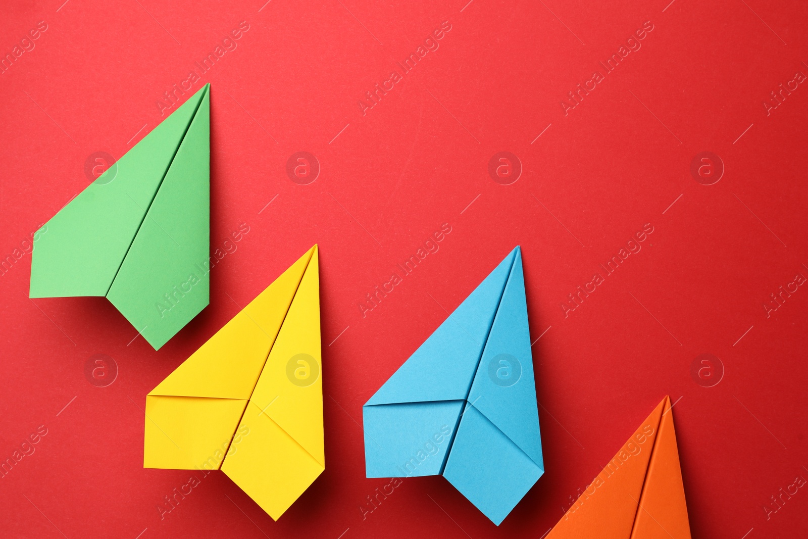Photo of Handmade colorful paper planes on red background, flat lay. Space for text