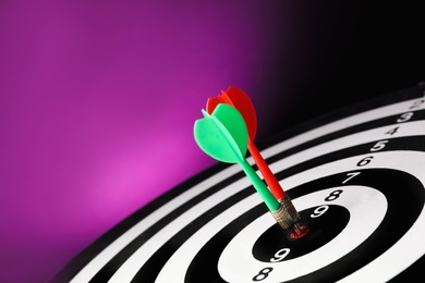 Photo of Arrows hitting target on dart board against purple background. Space for text