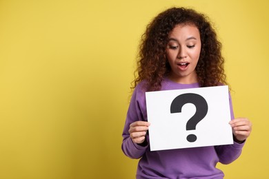Photo of Emotional African-American woman with question mark sign on yellow background. Space for text