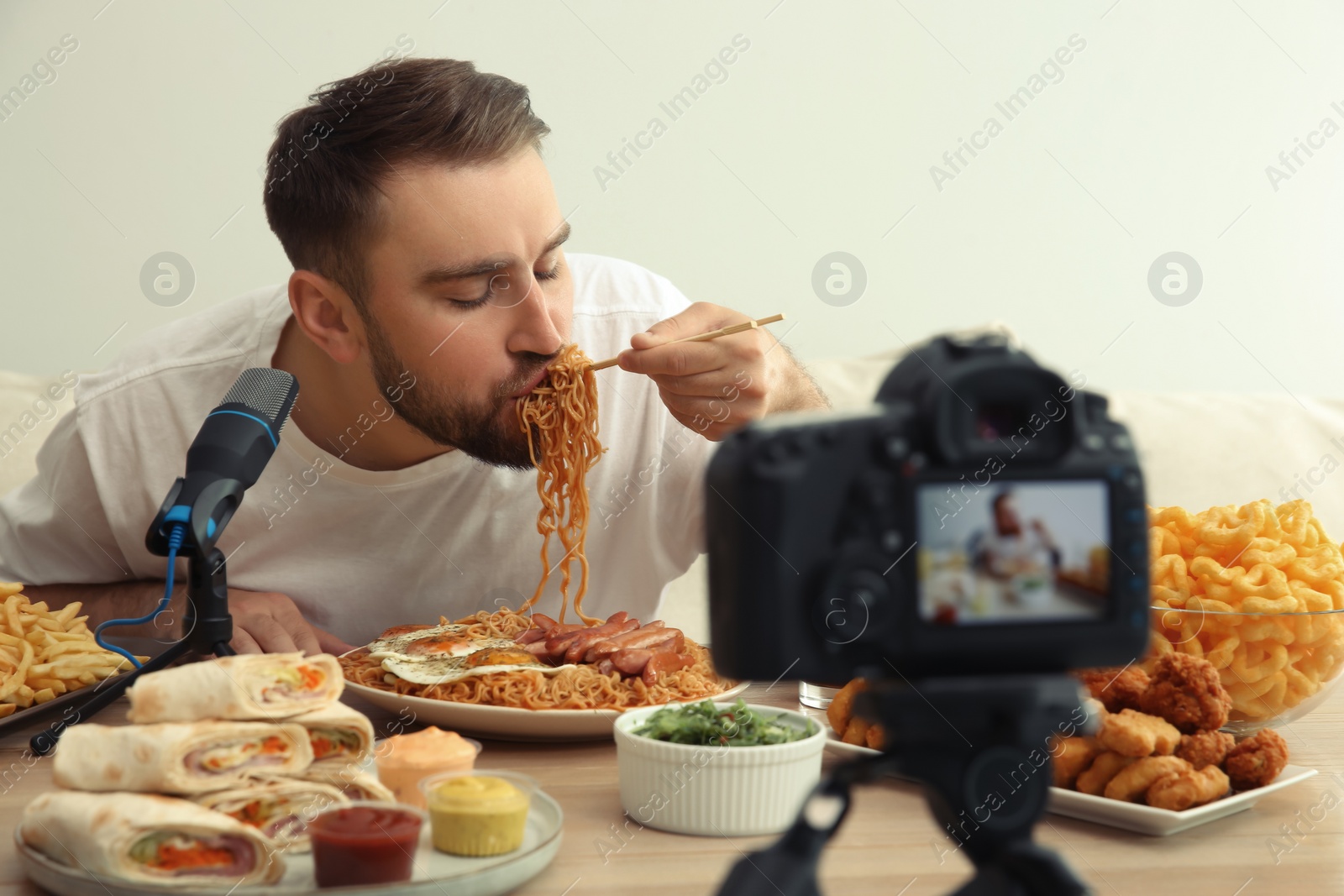 Photo of Food blogger recording eating show on camera against light background. Mukbang vlog