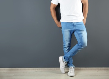 Photo of Young man in stylish jeans near grey wall with space for text, focus on legs