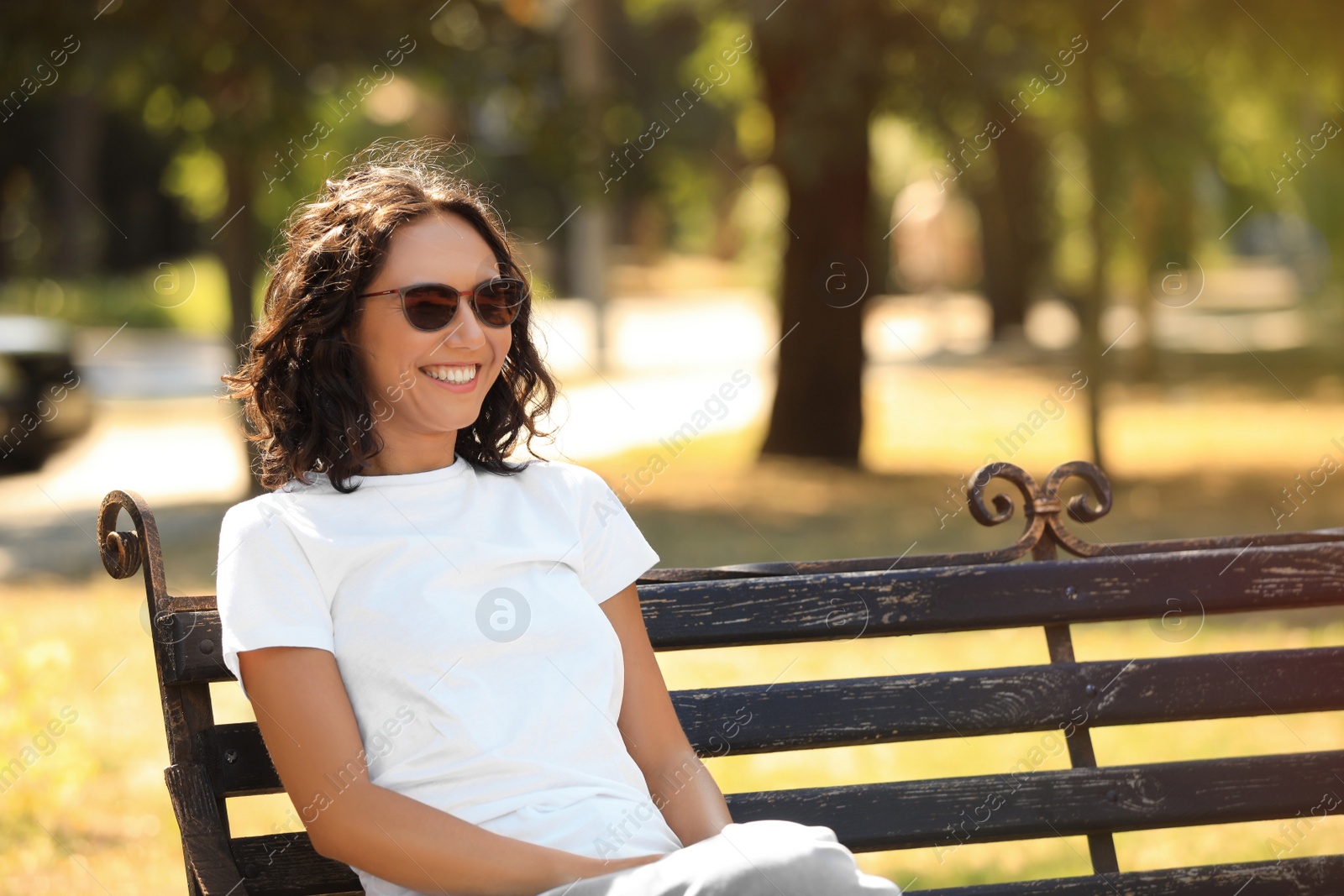 Photo of Happy young woman sitting on bench in park