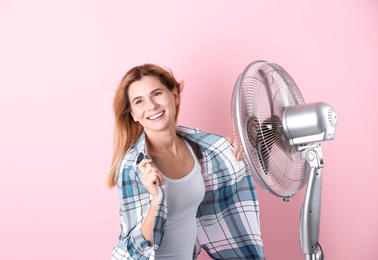 Woman refreshing from heat in front of fan on color background