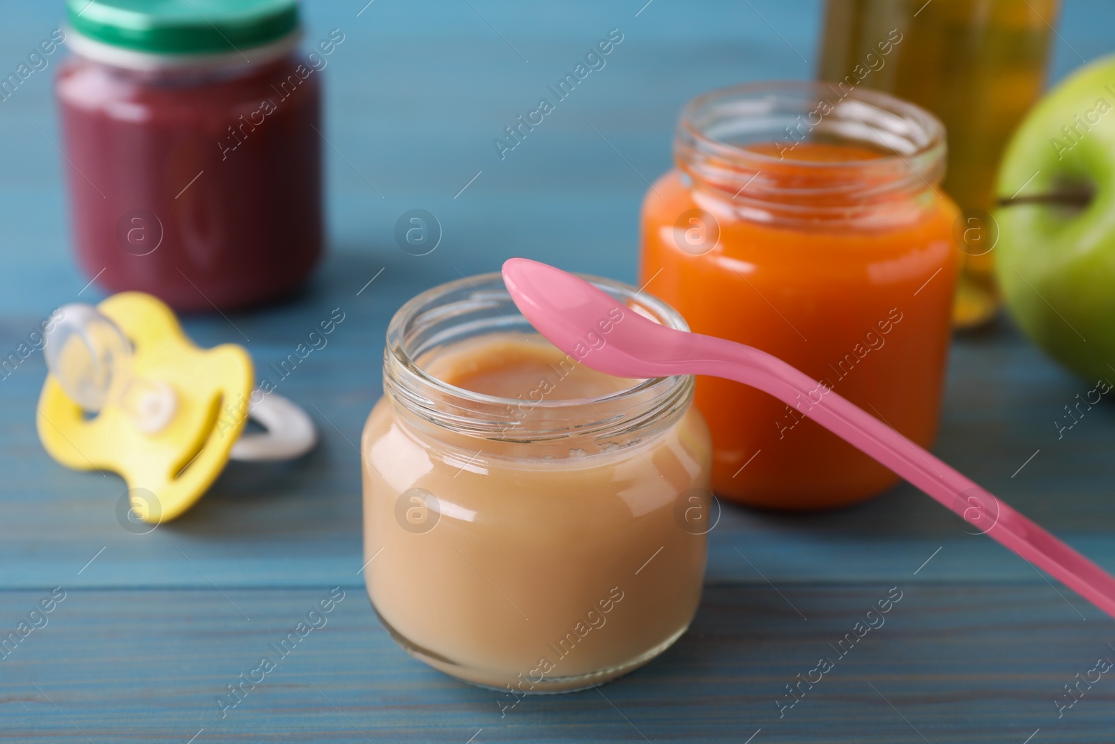 Photo of Jars with healthy baby food, bottle of juice, apple, spoon and pacifier on light blue wooden table