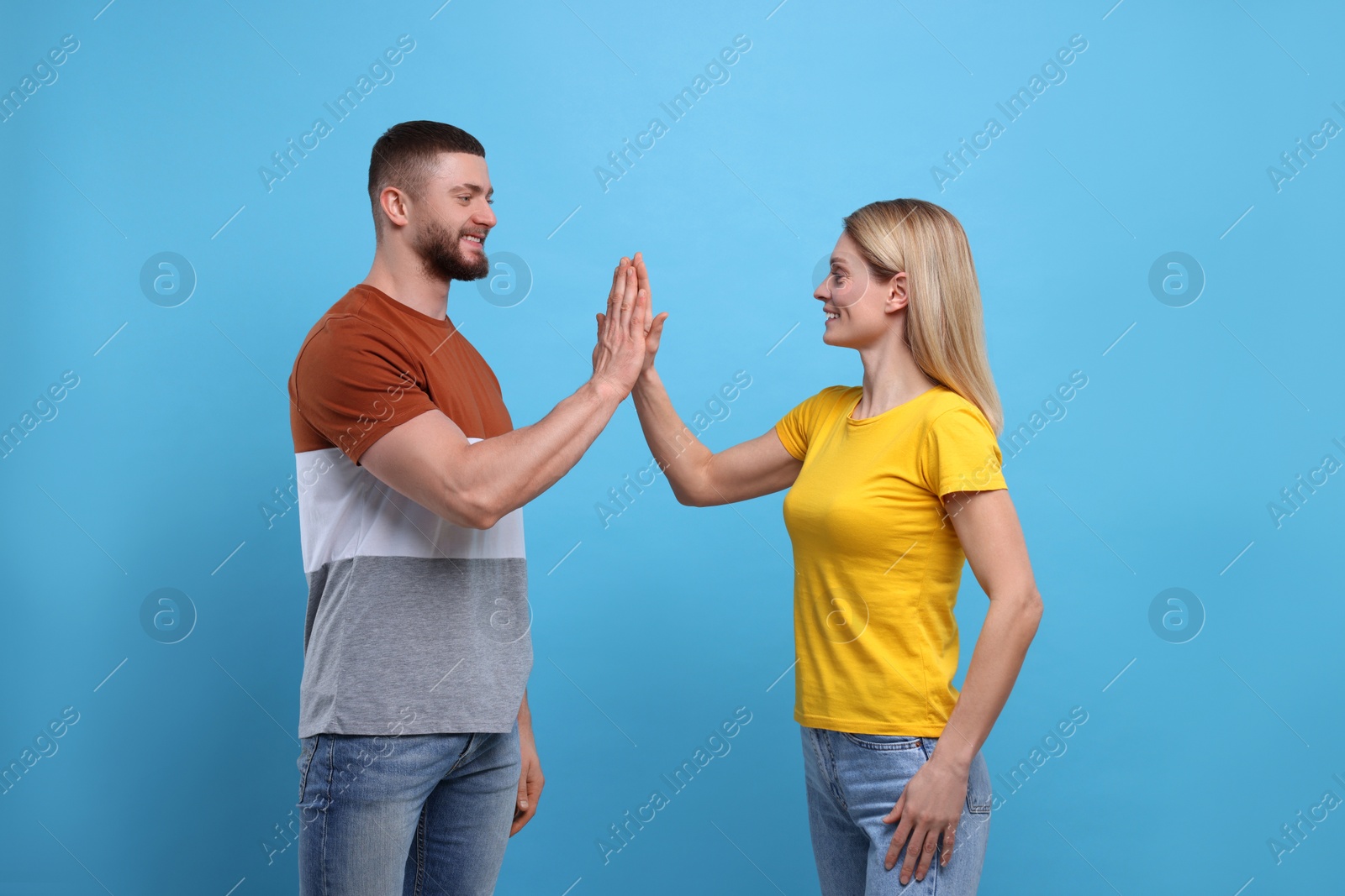 Photo of Happy couple giving high five on light blue background