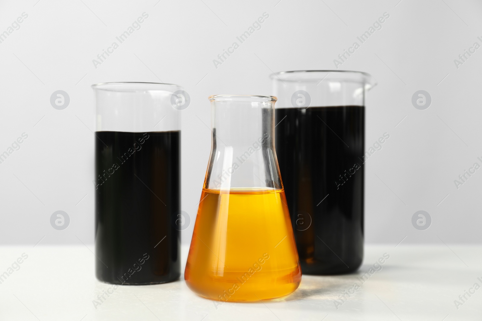 Photo of Beakers and flask with different types of oil on white table