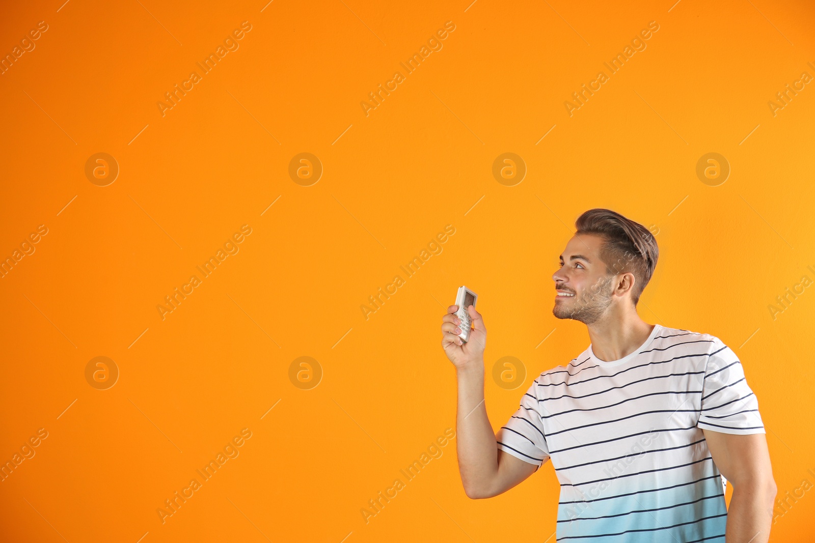 Photo of Young man with air conditioner remote on color background