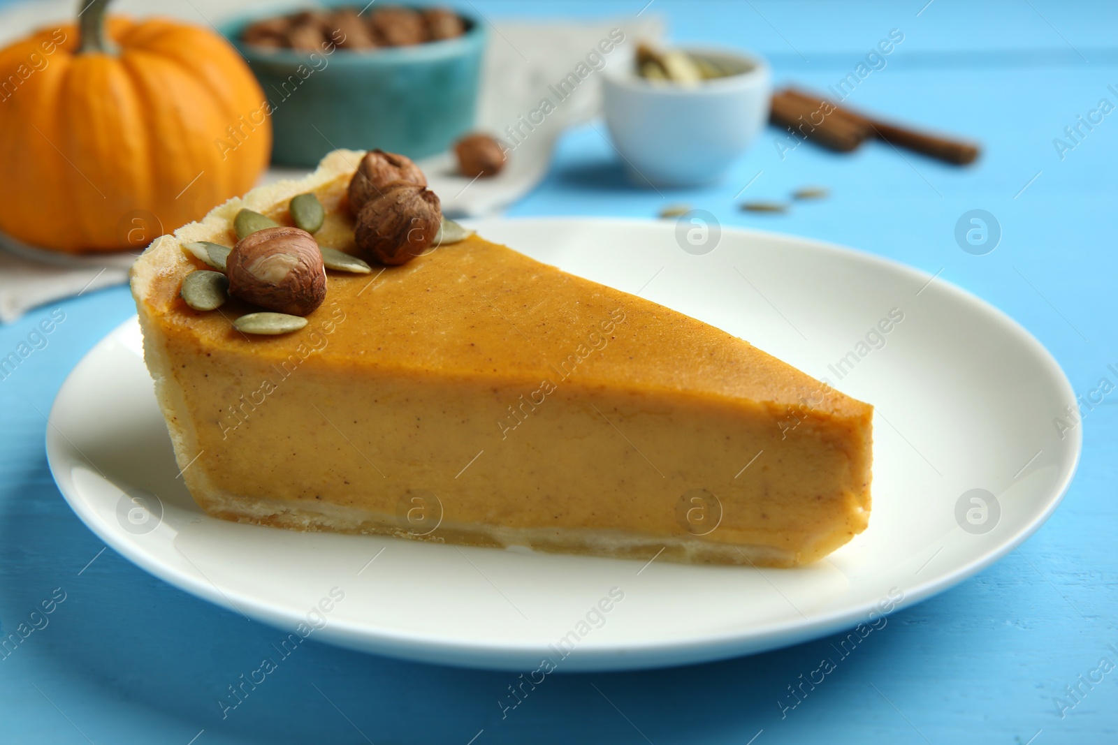 Photo of Piece of delicious pumpkin pie with hazelnuts and seeds on light blue wooden table, closeup