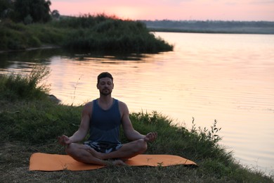 Photo of Man meditating near river in twilight. Space for text