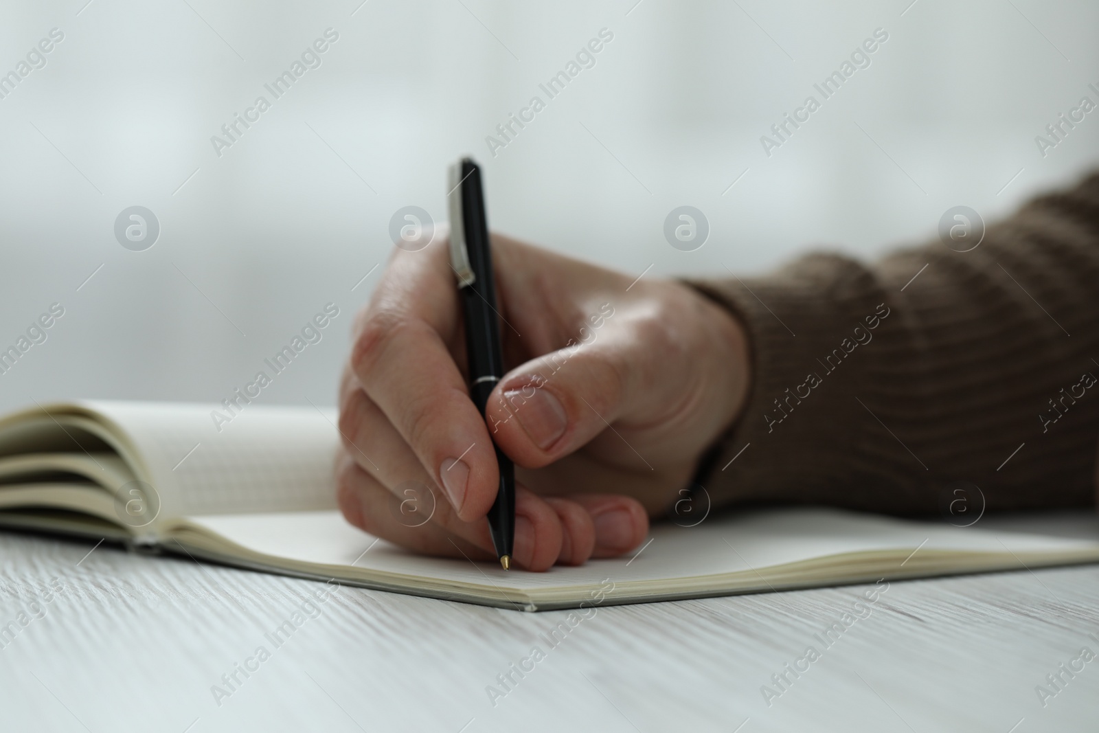 Photo of Man writing in notebook at white wooden table, closeup