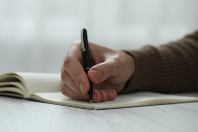 Photo of Man writing in notebook at white wooden table, closeup