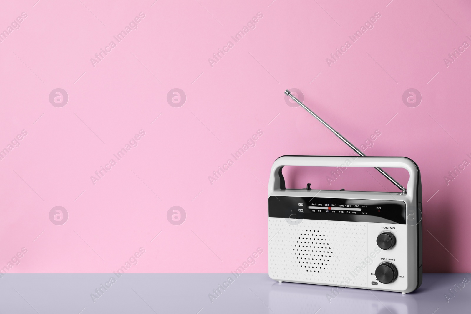 Photo of Retro radio receiver on table against pink background. Space for text