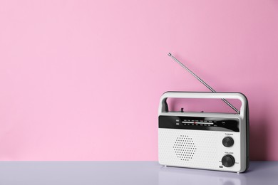 Photo of Retro radio receiver on table against pink background. Space for text
