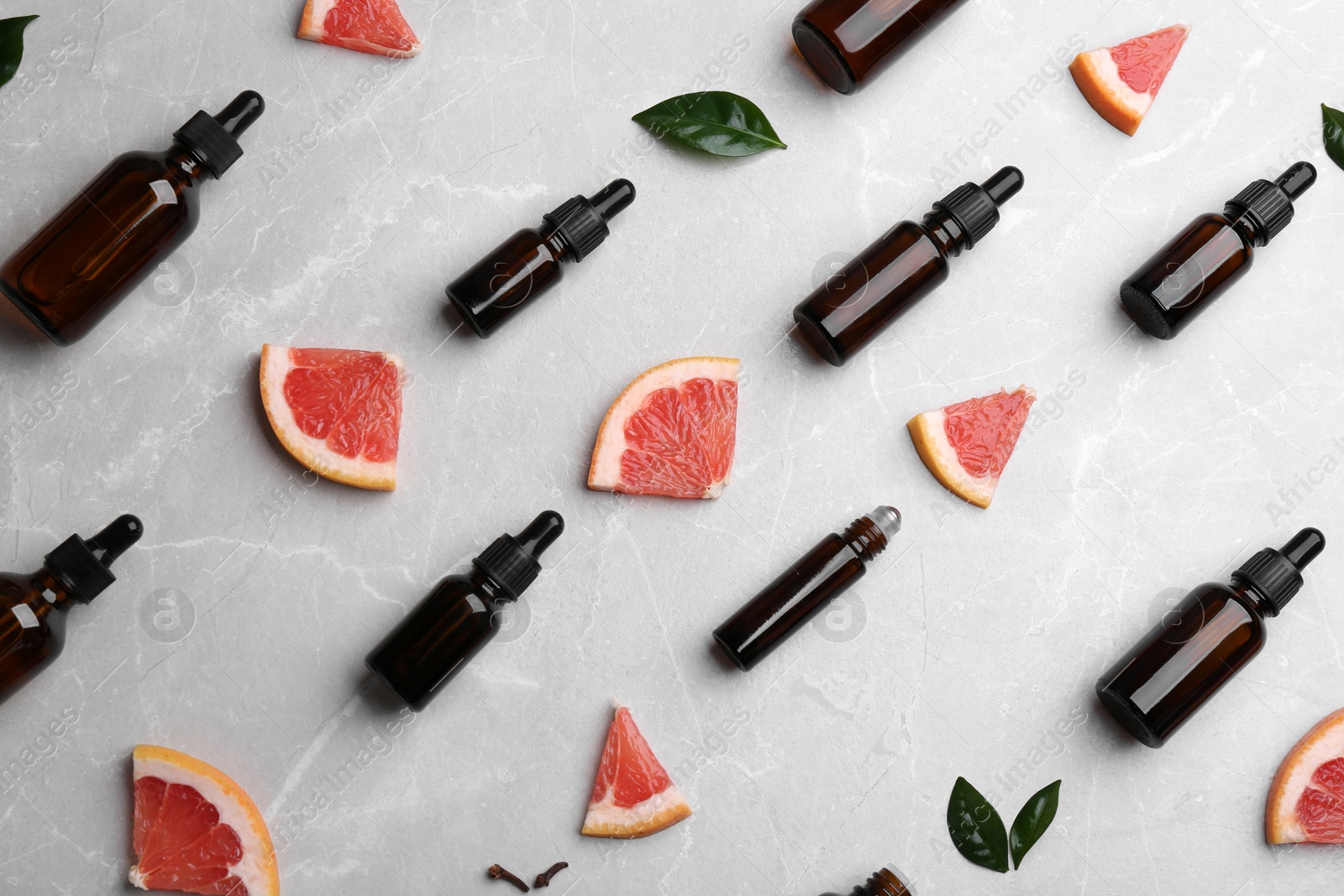 Photo of Flat lay composition with grapefruit slices and bottles of essential oil on grey background