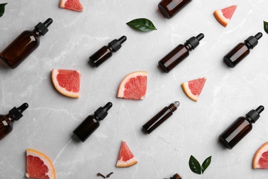 Flat lay composition with grapefruit slices and bottles of essential oil on grey background