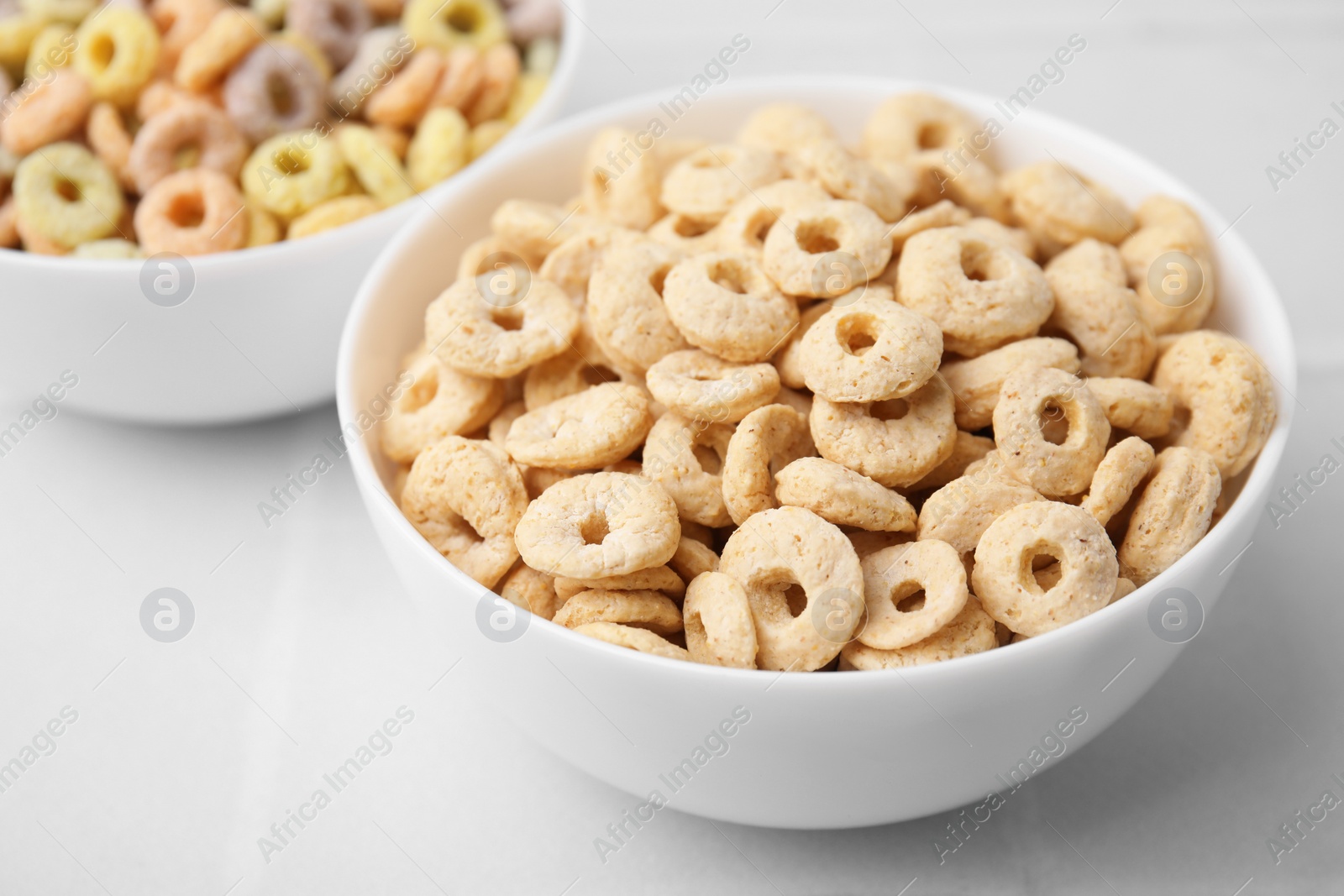 Photo of Tasty cereal rings in bowls on white table, closeup