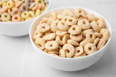 Photo of Tasty cereal rings in bowls on white table, closeup