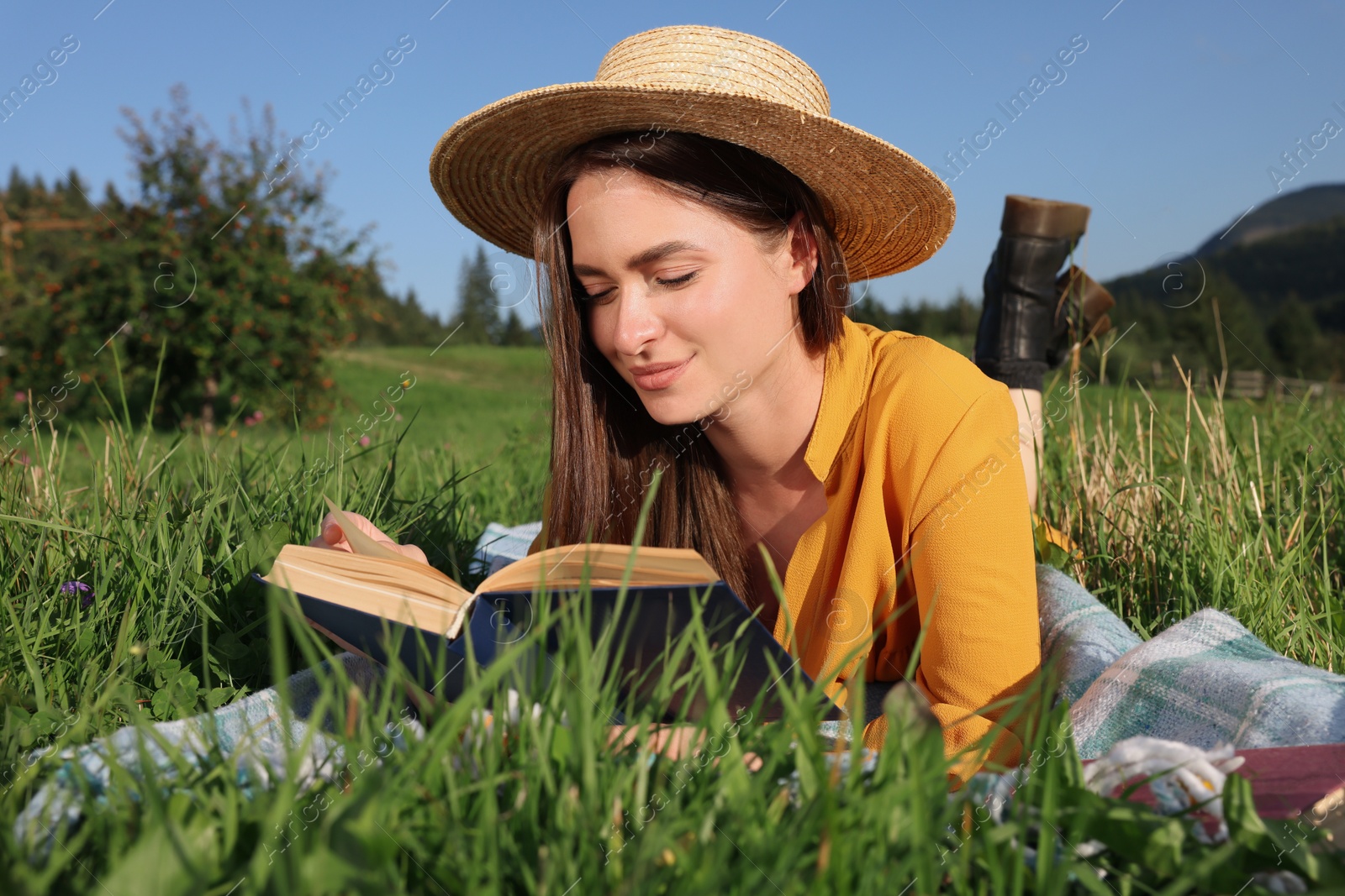 Photo of Beautiful young woman reading book on green meadow