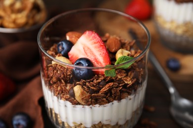 Photo of Tasty granola with berries, nuts and yogurt in glass on table, closeup