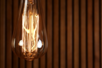 Lamp bulb near wooden wall, space for text