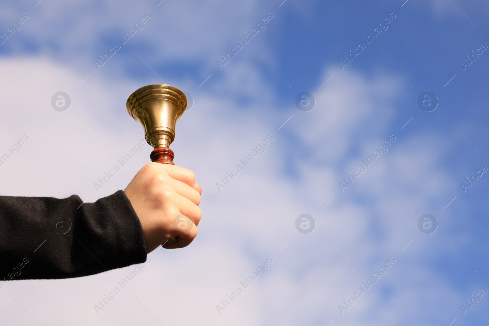 Photo of Pupil with school bell against cloudy sky, closeup. Space for text