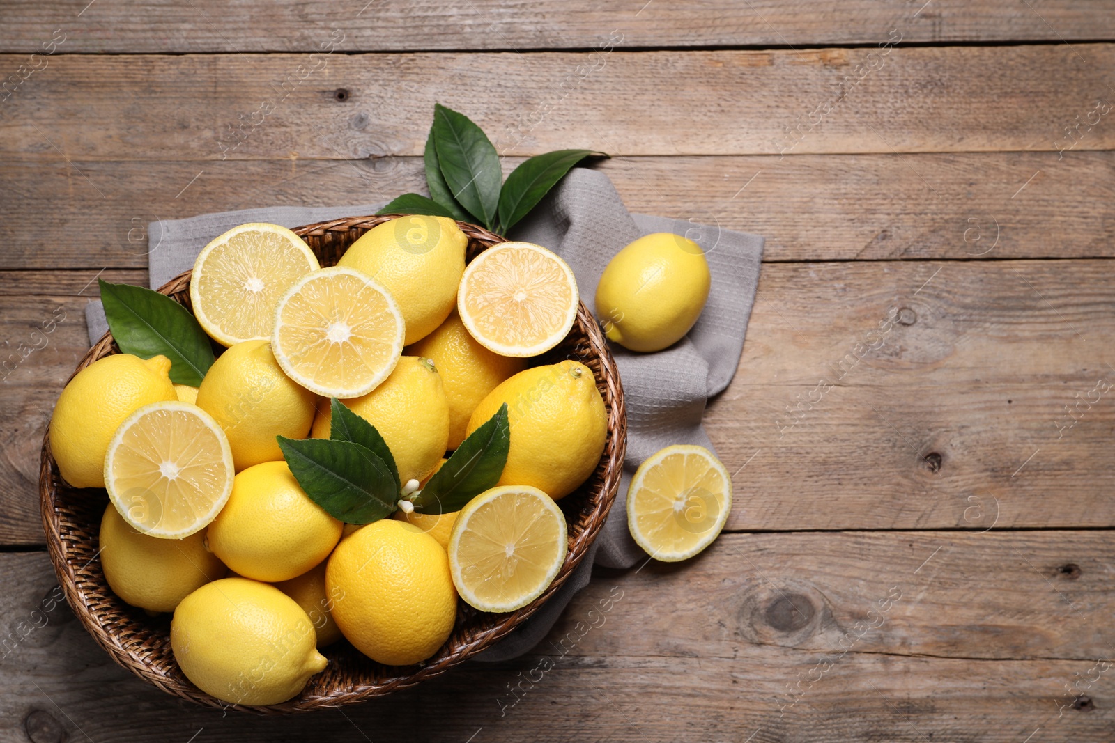 Photo of Many fresh ripe lemons with green leaves on wooden table, flat lay. Space for text