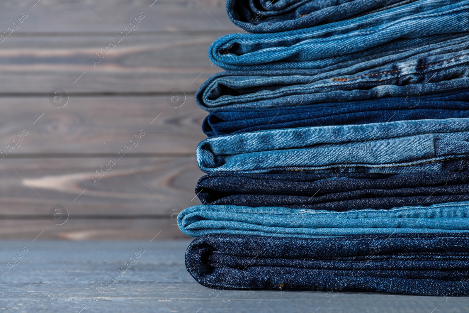 Photo of Stack of different jeans on grey wooden table, closeup