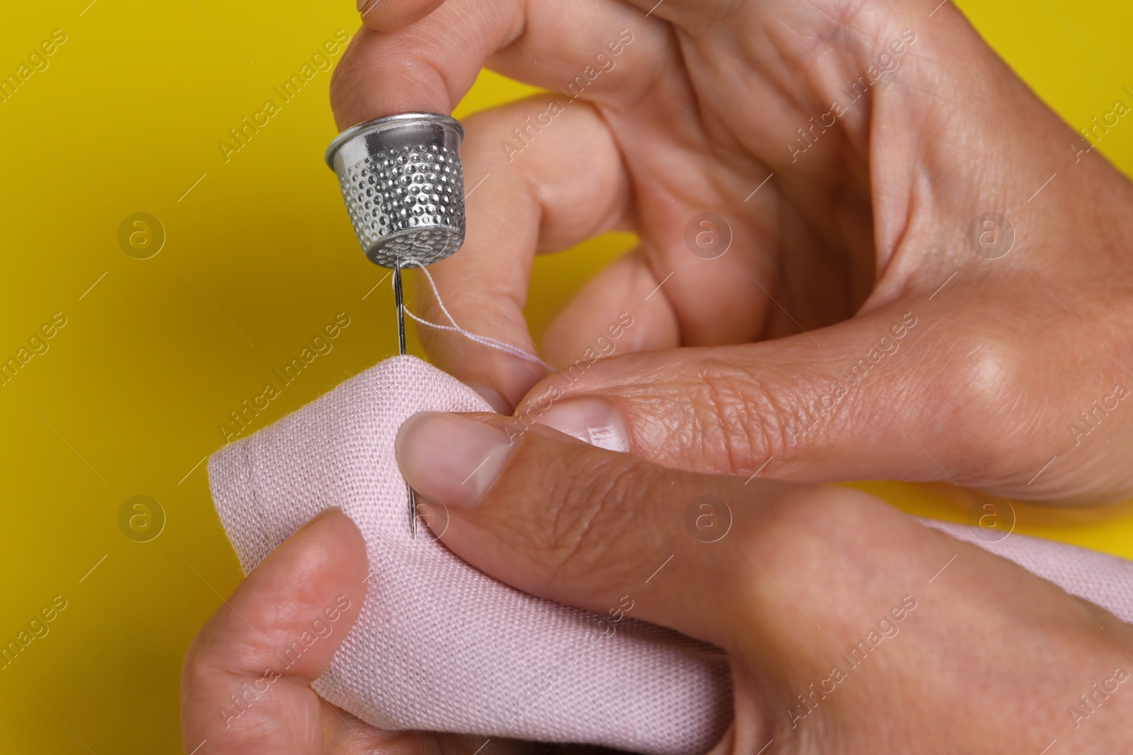 Photo of Woman sewing on fabric with thimble and needle against yellow background, closeup